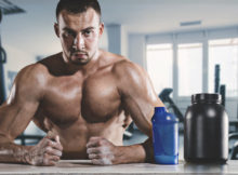 Muscular man sitting sweating in gym with drinking cup and supplement.